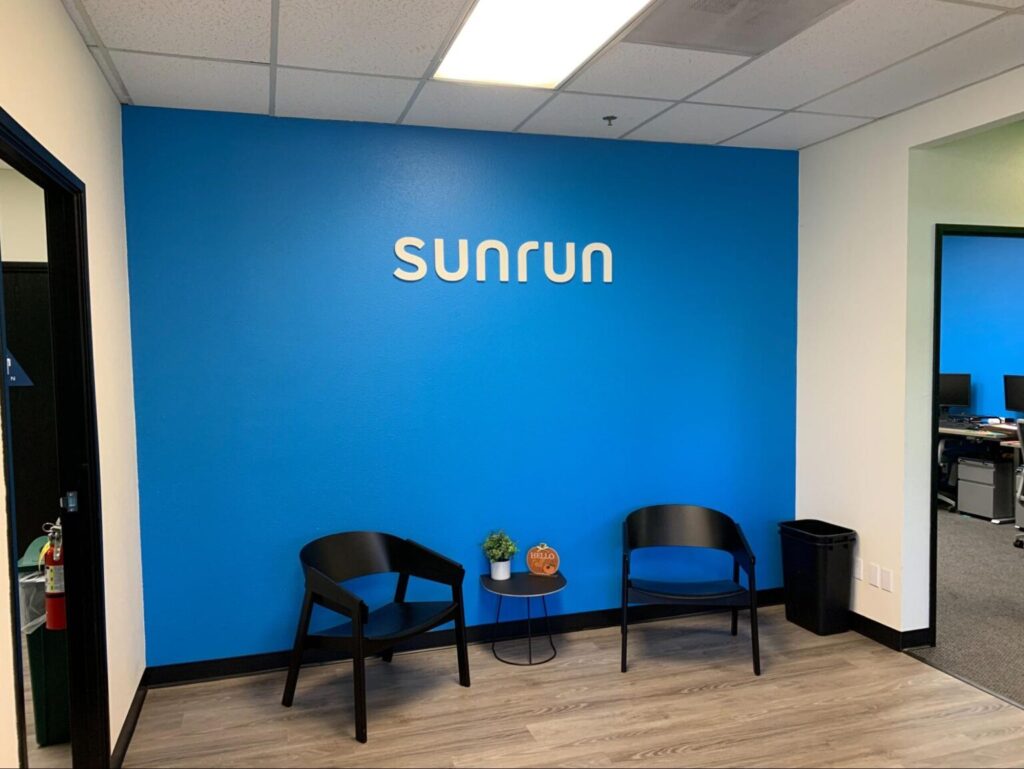 a white foam letter “sunrun” sign on a blue wall