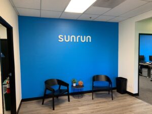 a white foam letter “sunrun” sign on a blue wall