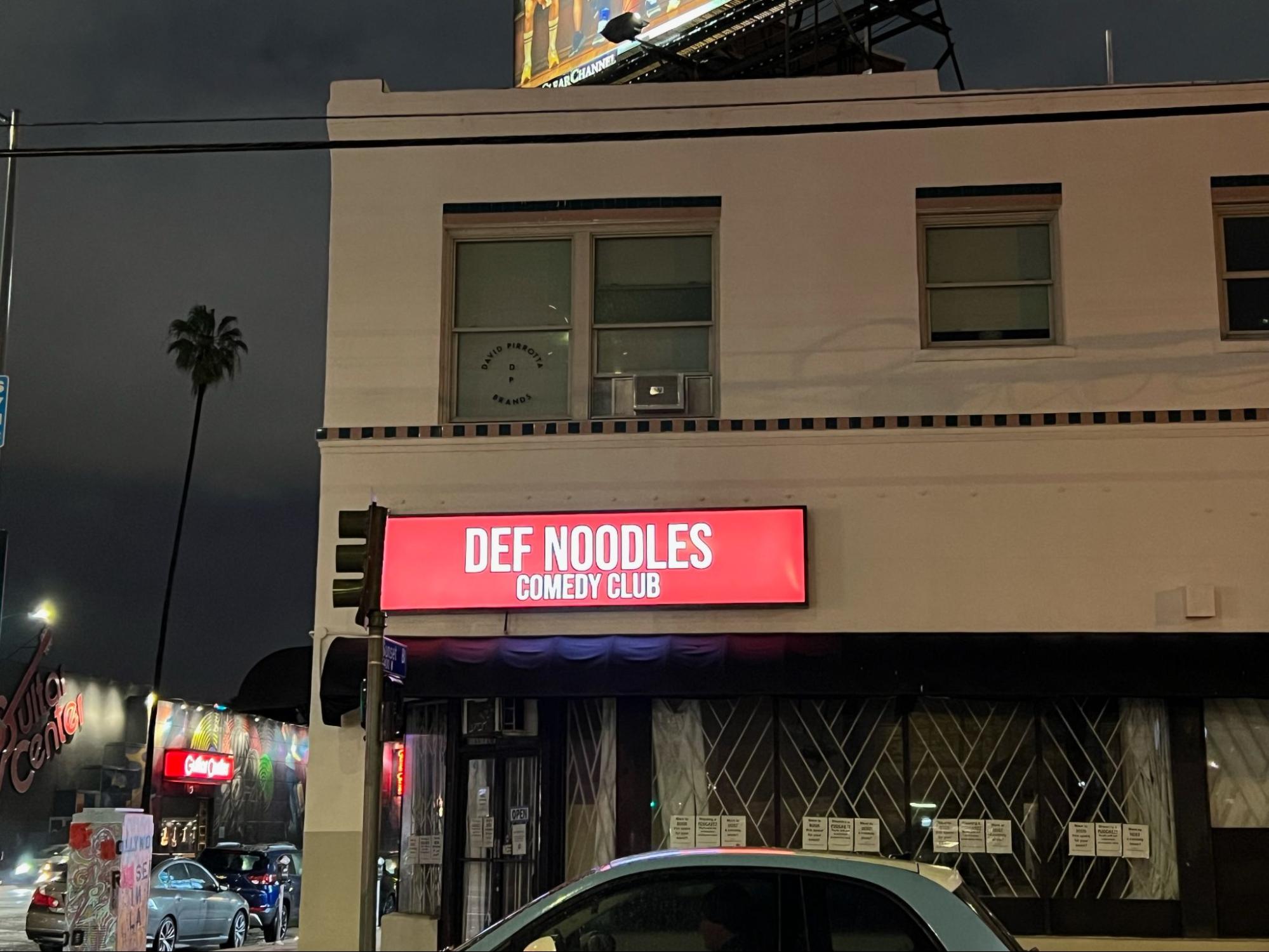 A lighted box sign for Def Noodles.